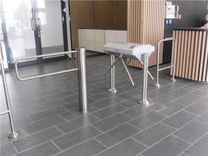 Modernes und sicheres Eingangsdesign: Eine Fusion aus Metalldrehkreuz, Geländer-Fuer-Zugangssystemen, grauen Fliesen und Holzwandverkleidung
