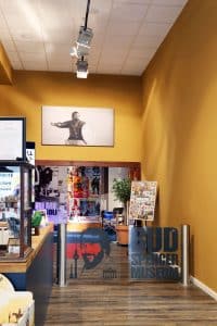 Treten Sie ein in die Welt von Bud Spencer: Ein Blick in den Innen- und Eingangsbereich des Bud Spencer Museums in Berlin mit zahlreichen Exponaten und einem besonderen gerahmten Foto, das die Besucher durch eine Glasdrehtür begrüßt