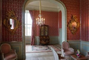 Erleben Sie zeitlose Eleganz in einem Raum mit rot gemusterter Tapete, antiken Möbeln, dekorativen Spiegeln und einem Kristallkronleuchter
