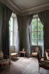 Gästehaus der Bundesregierung Schloss Meseberg: Erleben Sie die klassische Eleganz: Antikmöbliertes Zimmer mit hohen Fenstern und Blick auf die üppige grüne Landschaft